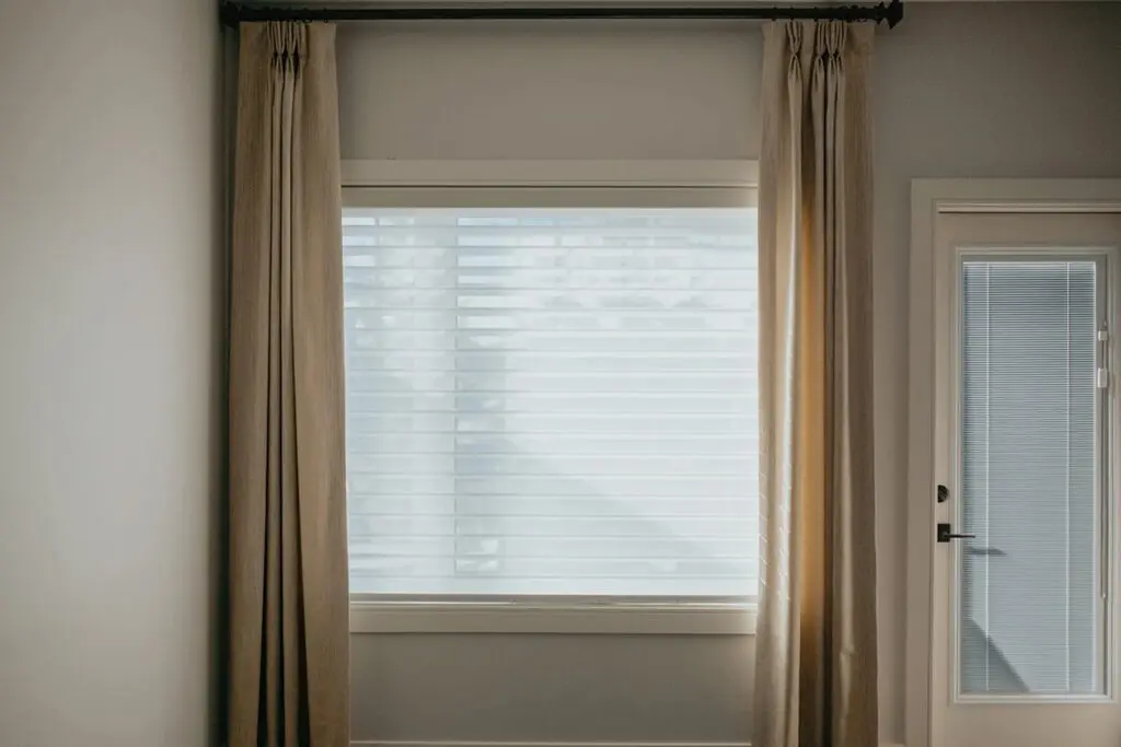 White Shangri-La sheer shade with open fabric vanes, framed by neutral drapes.